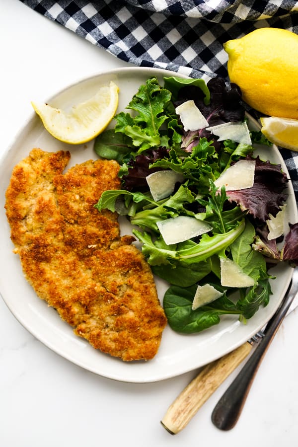 A plate of Pork Milanese with a salad and a wedge of lemon on the side