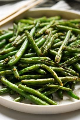 A plate of Asian Style green beans with chopsticks on the side