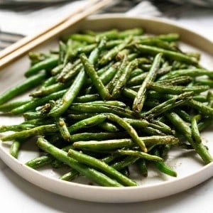 A plate of Asian Style green beans with chopsticks on the side