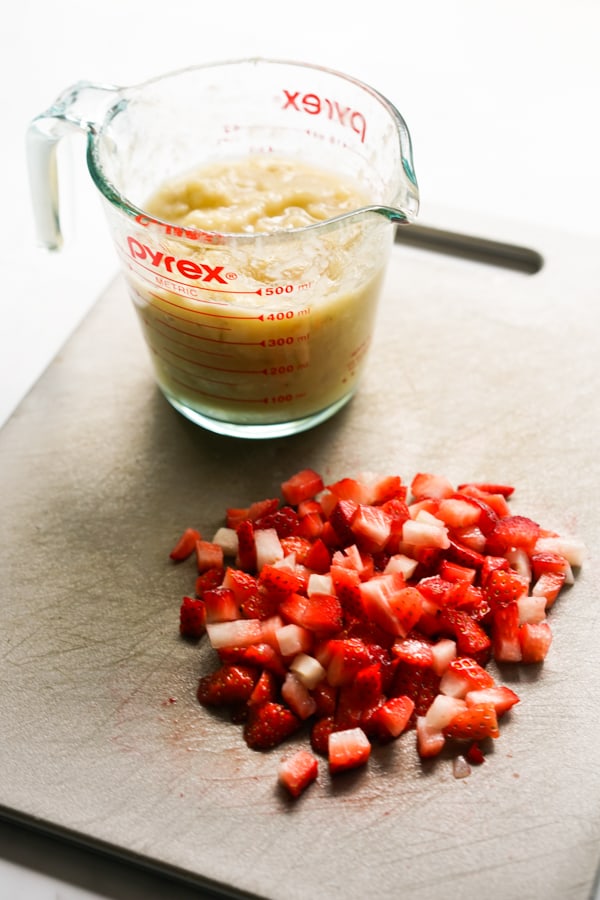 A cup of mashed bananas and sliced strawberries