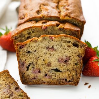 A slice of strawberry banana bread with the rest of the loaf in the background
