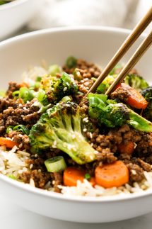 chopsticks digging into a bowl of ground beef bowl with rice and veggies