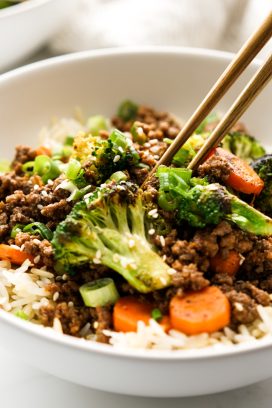 chopsticks digging into a bowl of ground beef bowl with rice and veggies