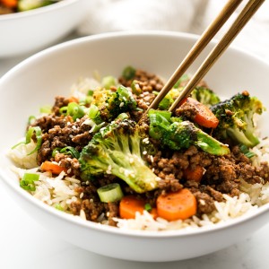 chopsticks digging into a bowl of ground beef bowl with rice and veggies