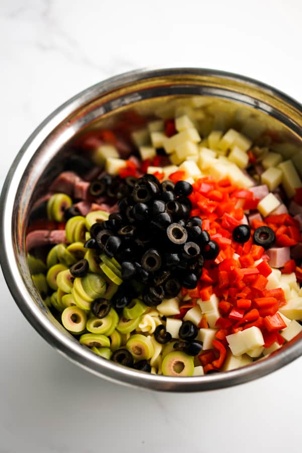 Pasta, olives, ham, salami, bell peppers in a large mixing bowl