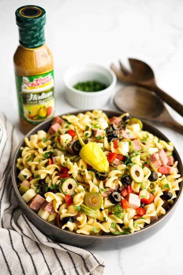 A bowl of pasta salad with Italian dressing in the background