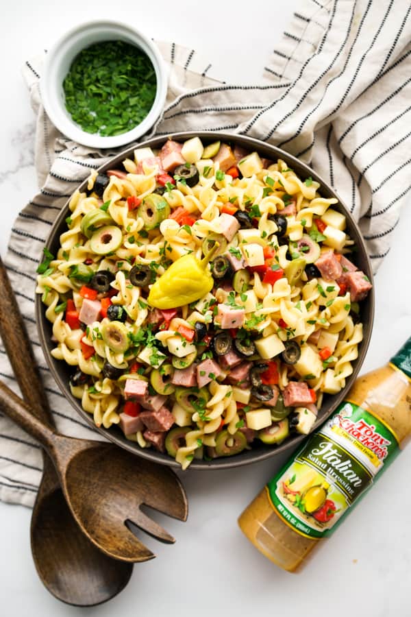 Top down view of a pasta salad in a large bowl, with Italian dressing and  wooden serving spoons around it