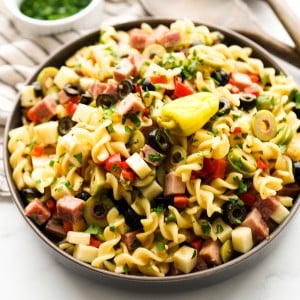 A bowl of pasta salad with ham, salami, olives and cubed cheeses