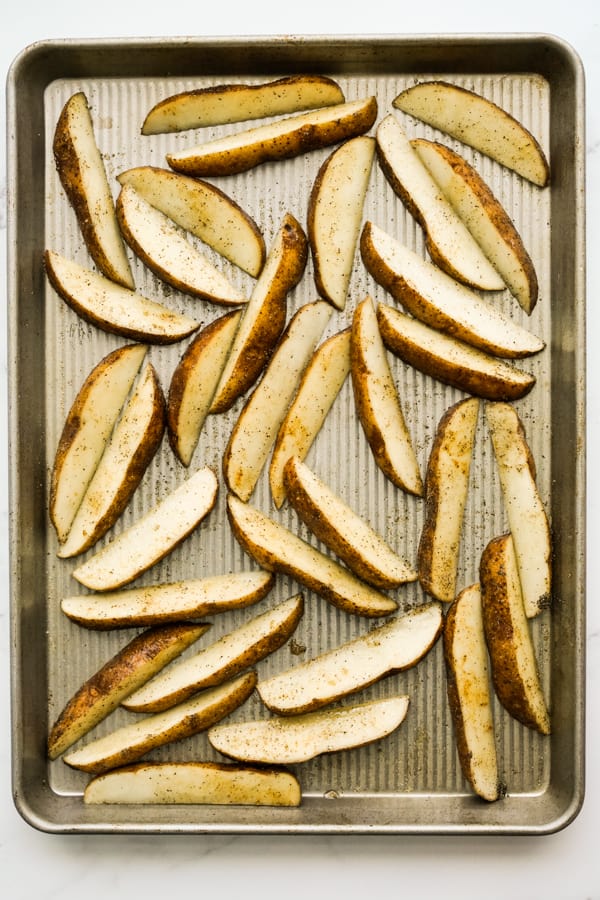 Potato wedges spread out on baking sheet