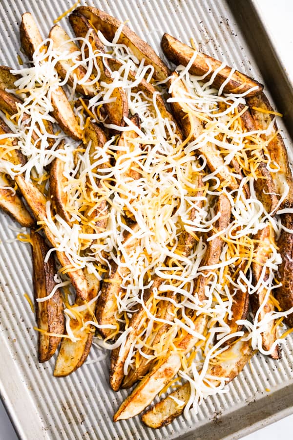 Baked Potato Wedges topped with shredded mozzarella and cheddar on a baking sheet