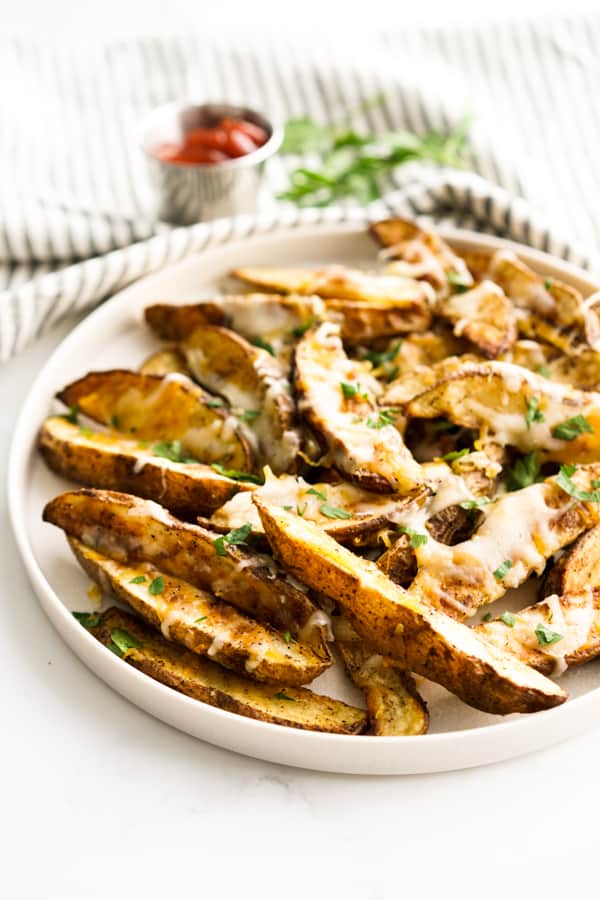 A plate of cheesy potato wedges with ketchup in the background