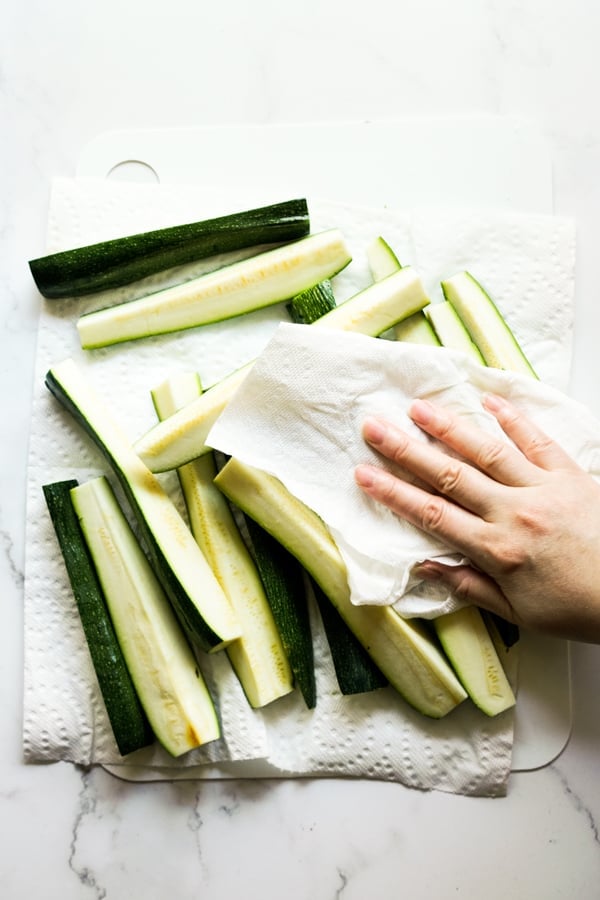 Using paper towel to dab on zucchini spears to remove moisture