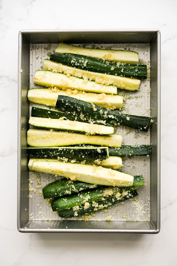 A rectangular dish filled with zucchini spears tossed in garlic and parmesan cheese