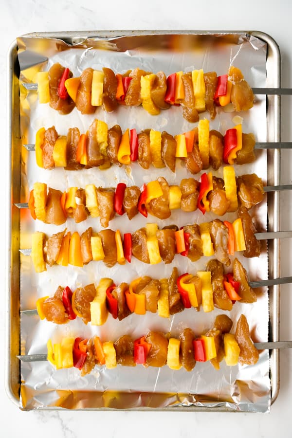 Uncooked chicken skewers along with bell peppers and pineapple