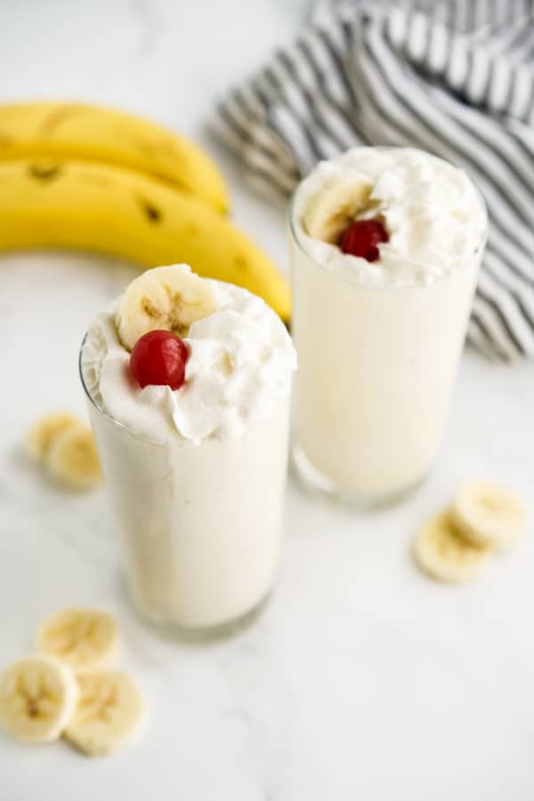Top down view of two tall glasses filled with banana milkshake with bananas in the background