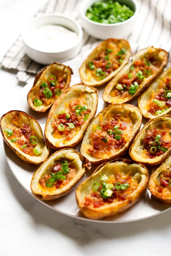 A plate of baked potato skins loaded with bacon and chives, served with sour cream on the side