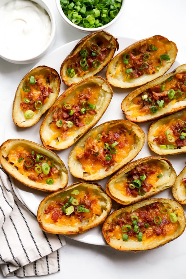 Top down view of a plate of Loaded Baked Potato Skins served with sour cream and green onions