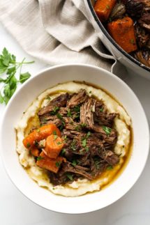 Top down view of a bowl with mashed potatoes and shredded pot roast, with a pot in the background