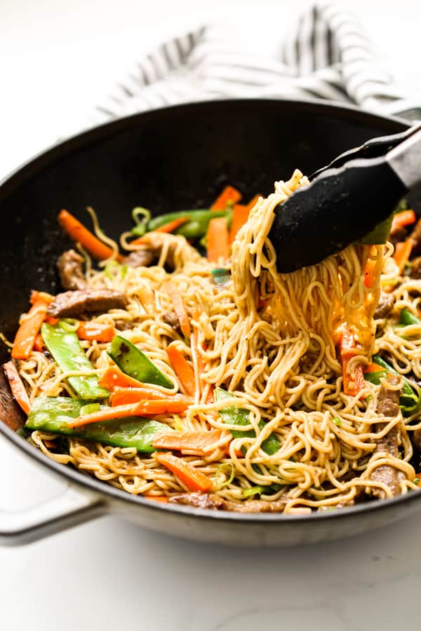 A large skillet of noodles tossed in sauce, along with beef and veggies