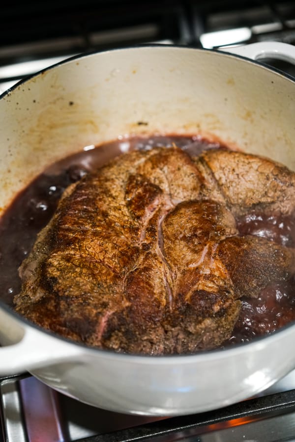 Beef chuck simmering in red wine in a large pot