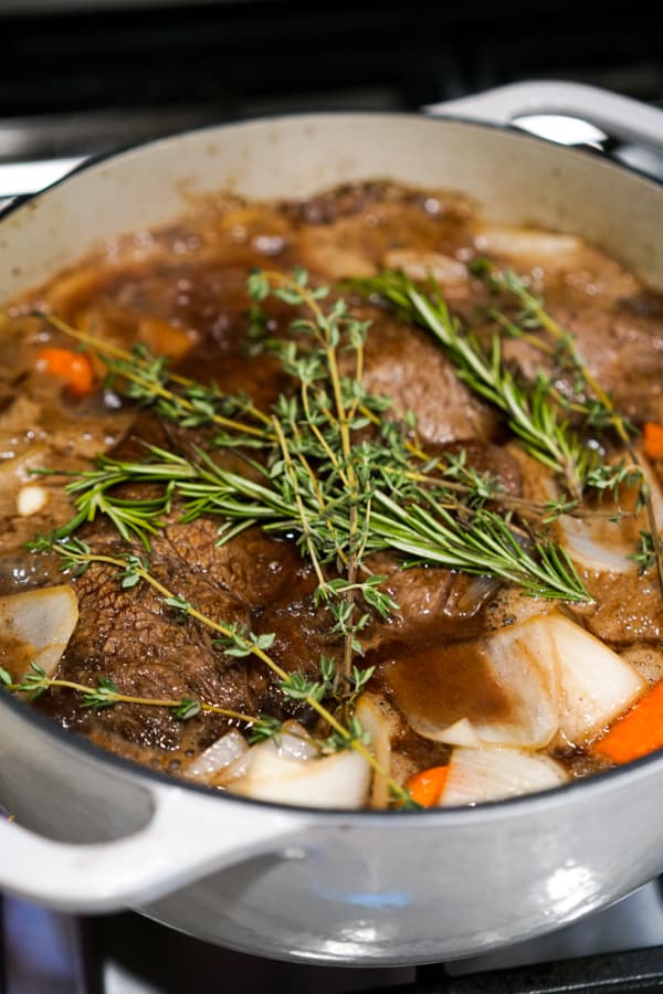 Fresh thyme and rosemary on top of a beef chuck cooking in a pot