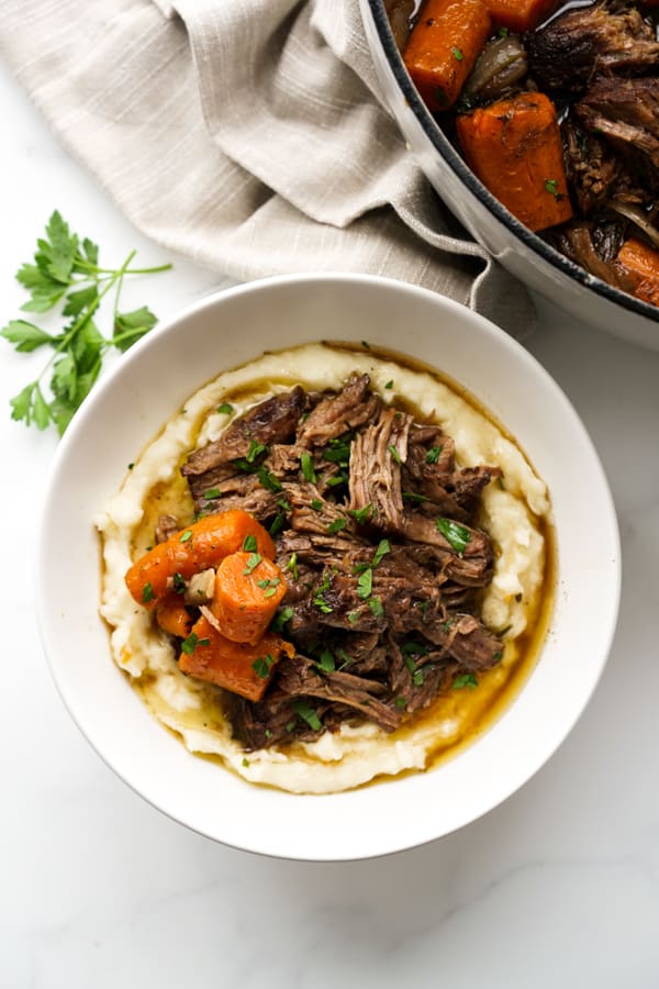 Top down view of a bowl with mashed potatoes and shredded pot roast, with a pot in the background