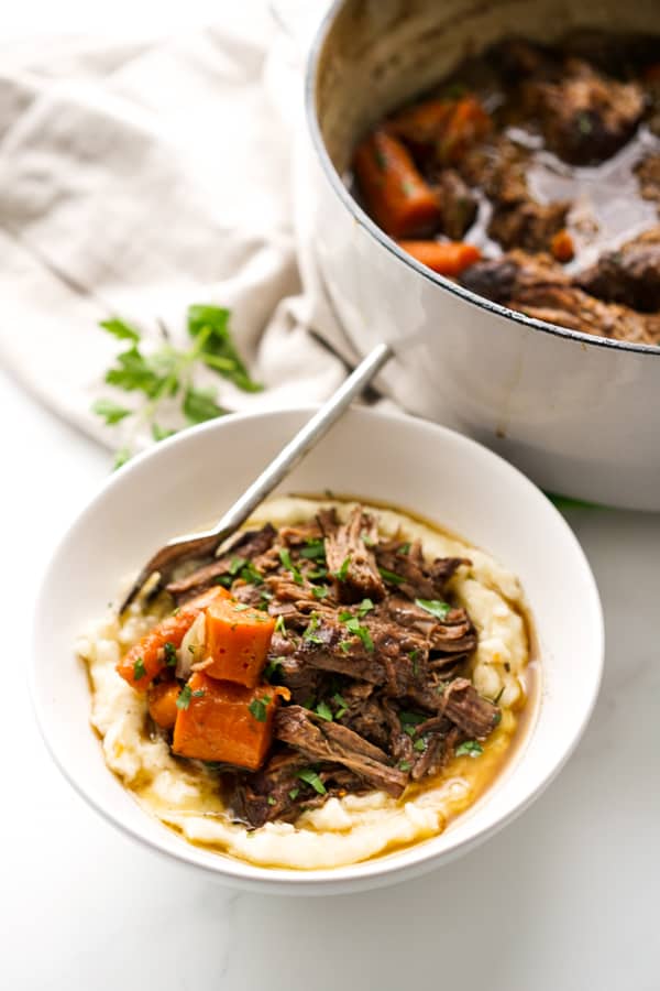 A bowl of shredded beef pot roast on top of mashed potatoes