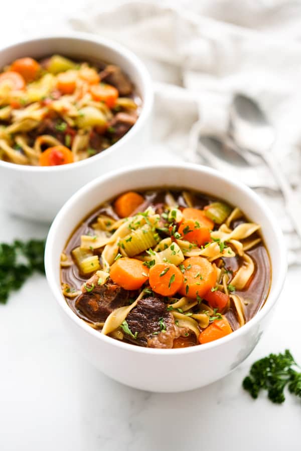 Two bowls of soup loaded with beef, egg noodles, carrots and celery.