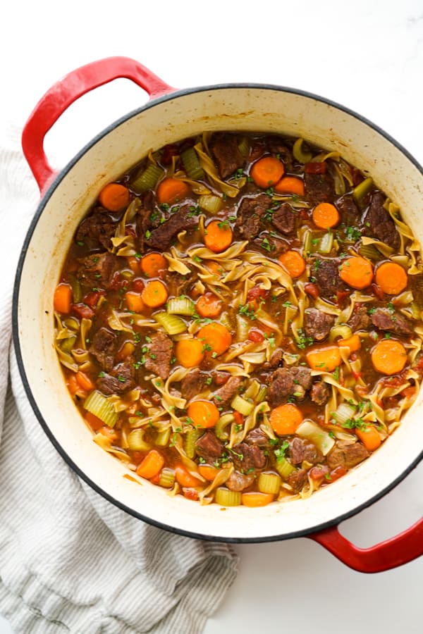 A large pot of Beef Noodle Soup with kitchen towel on the side