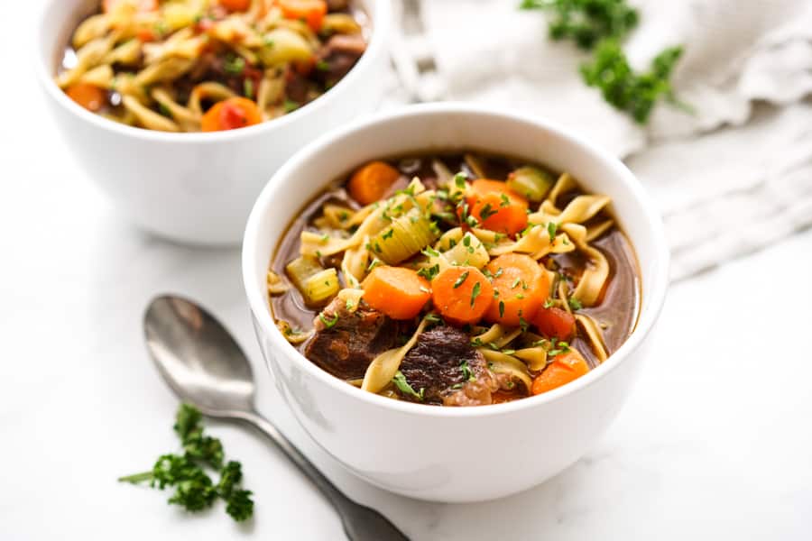 A bowl of beed noodle soup with carrots and chunks of steaks
