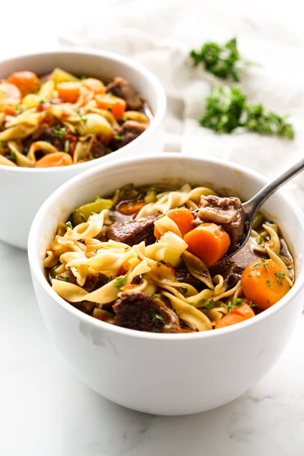 Using a spoon to scoop up some Beef Noodle Soup from a bowl