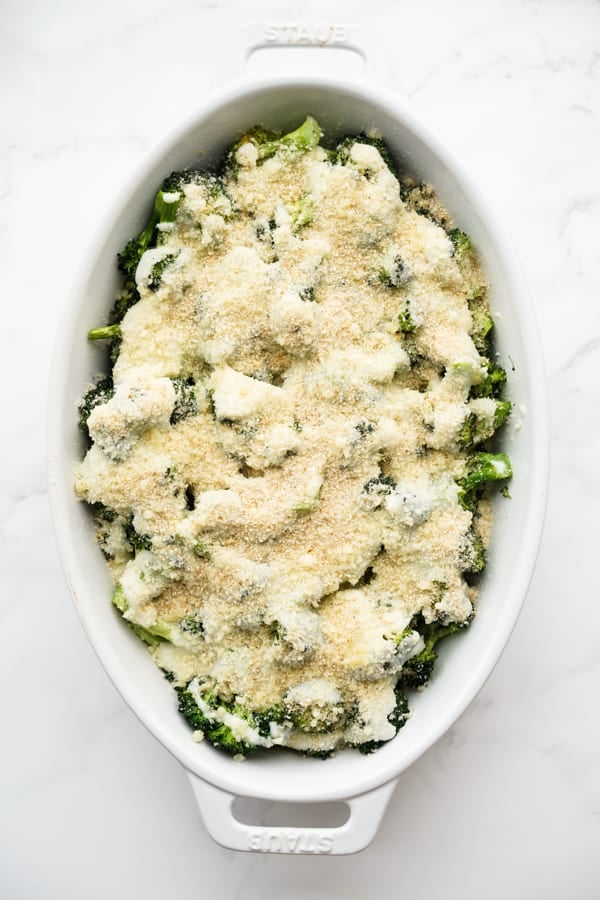 Broccoli in an oval casserole topped with cream sauce and then breadcrumbs and parmesan.