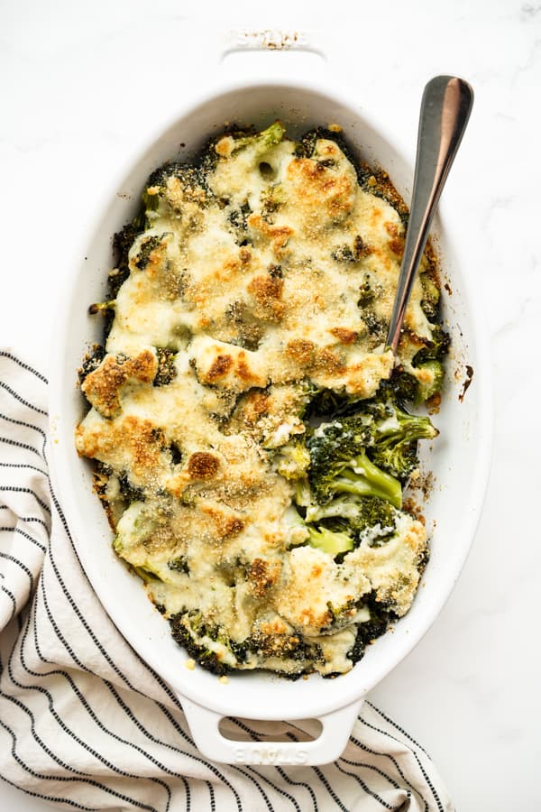 An oval gratin casserole loaded with broccoli and topped with creamy cheese sauce