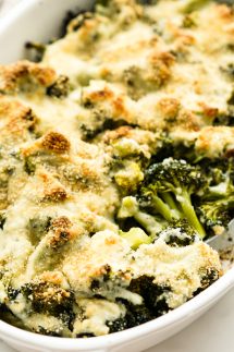 Scooping into a casserole dish loaded with broccoli topped with cream sauce and cheese