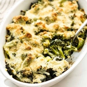 Scooping into a casserole dish loaded with broccoli topped with cream sauce and cheese