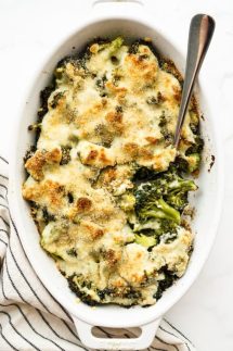 An oval gratin casserole loaded with broccoli and topped with creamy cheese sauce