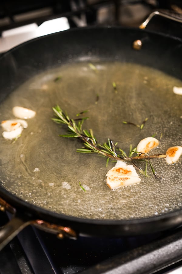 Cooking garlic cloves, herbs in white wine and chicken broth in the skillet