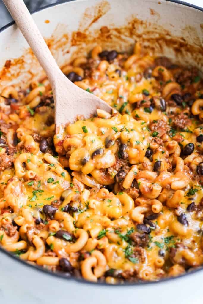 Scooping out some chili mac and cheese from a Dutch oven using a wooden spoon