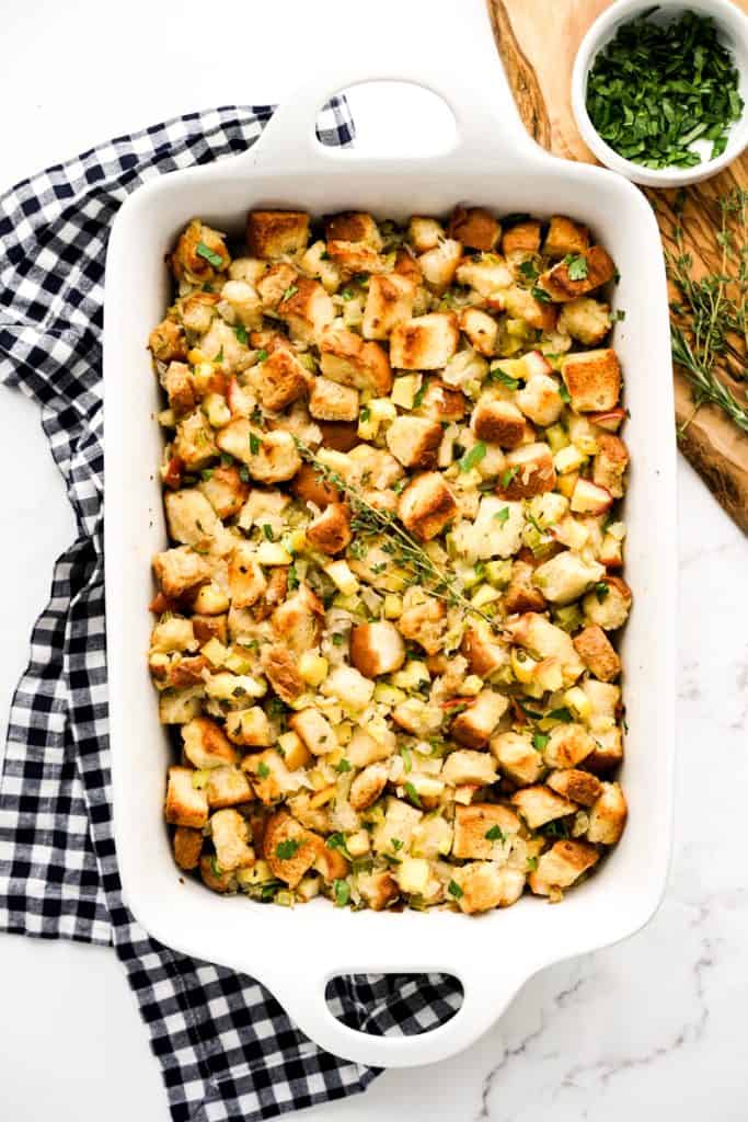 A rectangular baking dish loaded with toasted bread tossed in apple cubes, onions and celery.