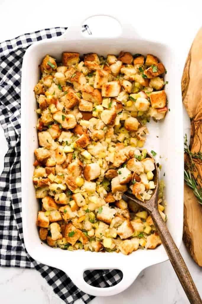 A spatula digging into a baking dish filled with apple onion celery stuffing