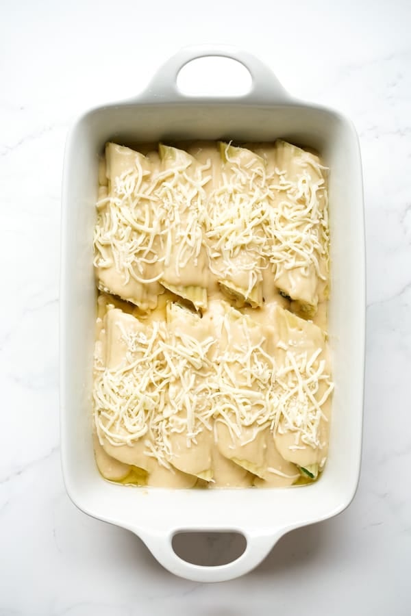 Top down view of a rectangular dish filled with stuff manicotti, topped with white sauce and shredded cheese