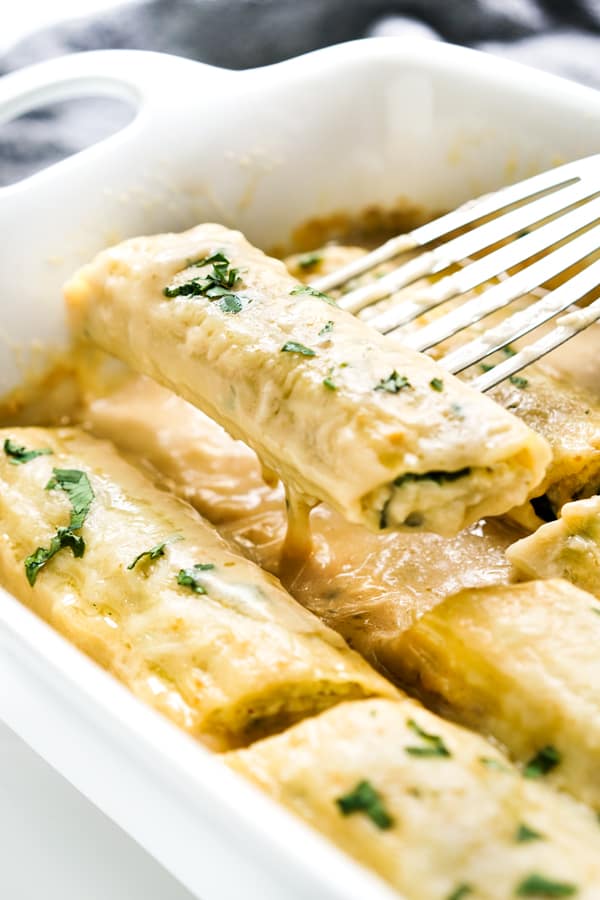 Lifting up one manicotti stuffed with chicken spinach and cheese out from the pan