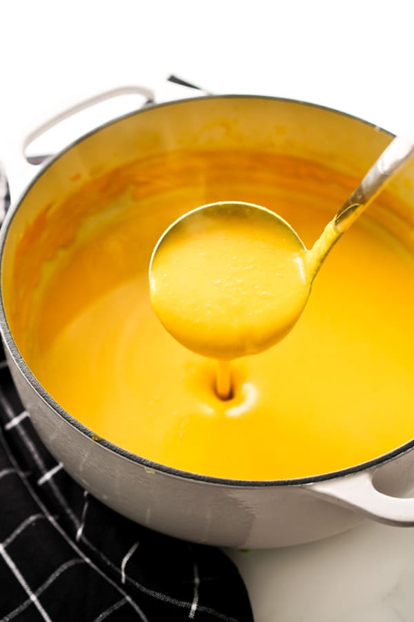 Using a ladle to scoop up Curry Butternut Squash Soup in a large Dutch oven