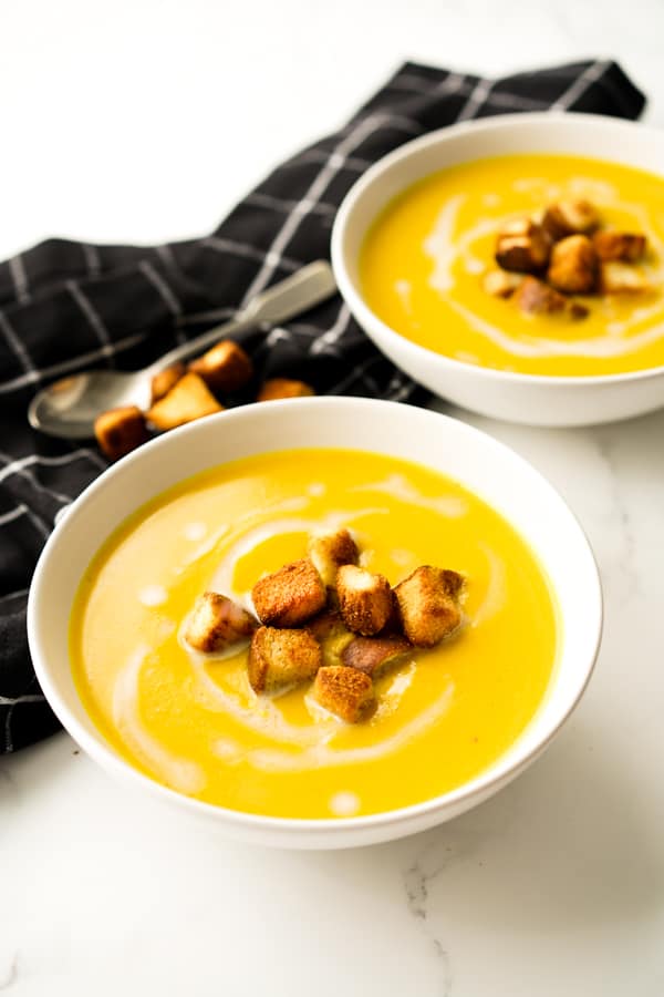 Two bowls of curry butternutsquash soup topped with croutons and coconut milk