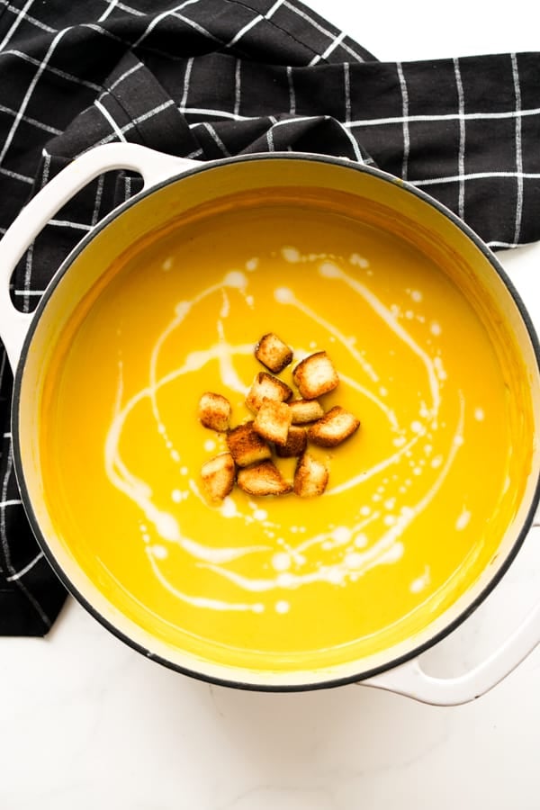 A large pot of curry butternut squash soup topped with croutons and drizzled with coconut milk