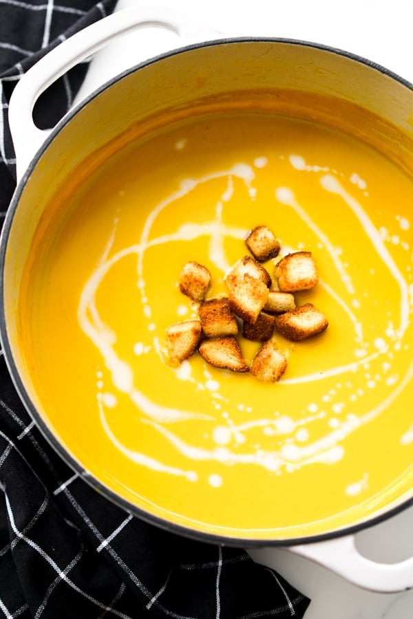 Closeup of a large pot of butternut squash curry soup with croutons and coconut milk swirls on top