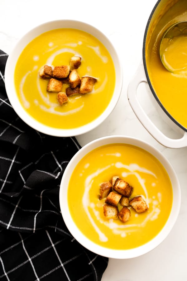 Top down views of two bowls of butternut squash soup with the pot next to it