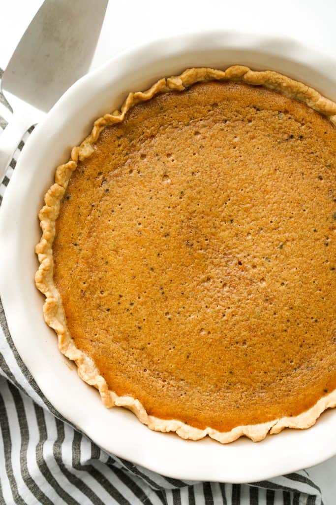 Pumpkin pie in a large pie pan with a serving spoon on the side