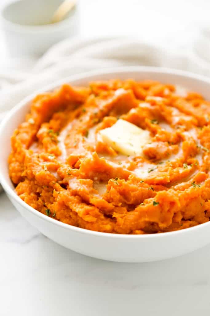 Mashed sweet potatoes in a big bowl with swirls on top along with melted butter