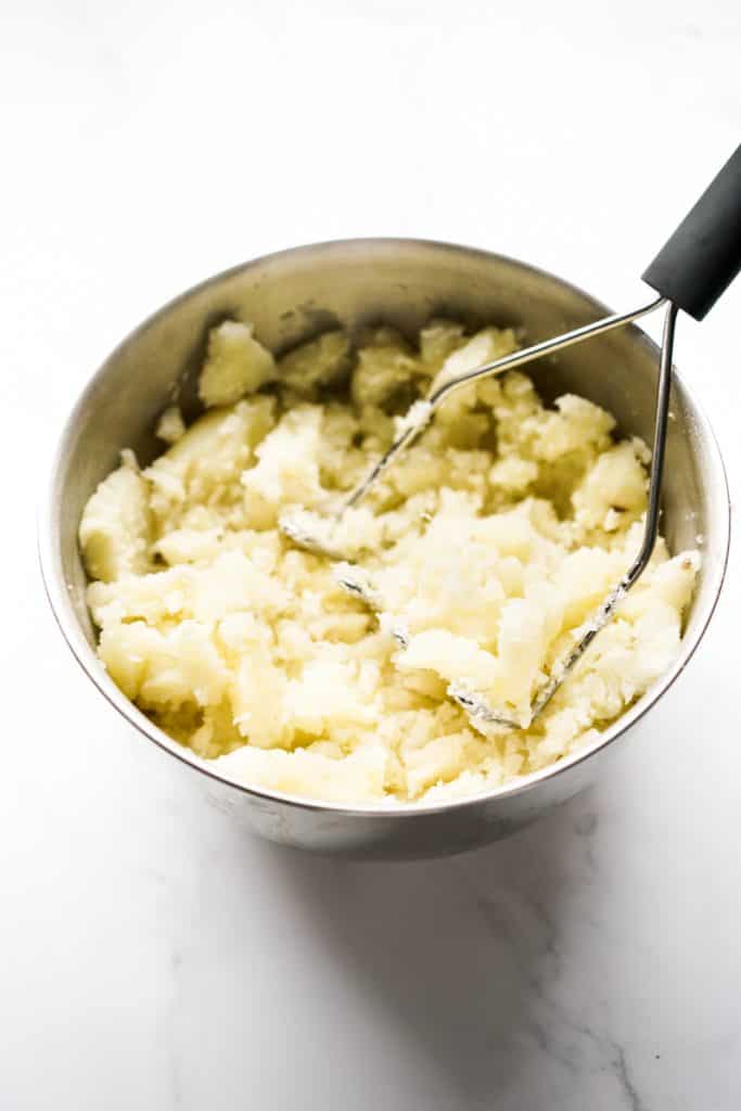 Using a potato masher to mash potatoes in a large mixing bowl